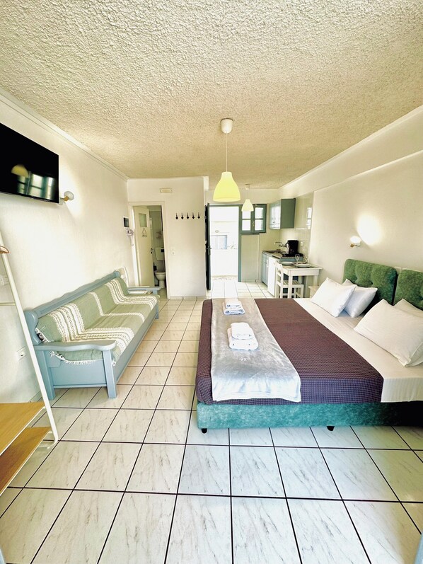 A hotel room with a bed, a sofa, a small table, and a television. - Zacharakis Studios (Santorini)