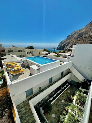 A rooftop pool with a view of the sea, surrounded by white buildings and greenery. - Zacharakis Studios (Santorini)