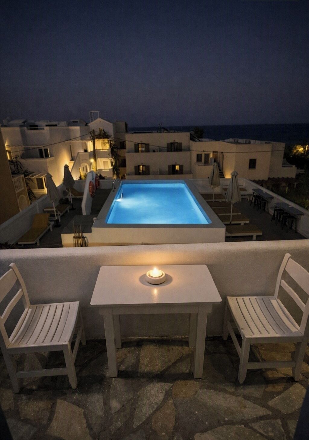 A rooftop pool area with a table and two chairs, surrounded by buildings with balconies.