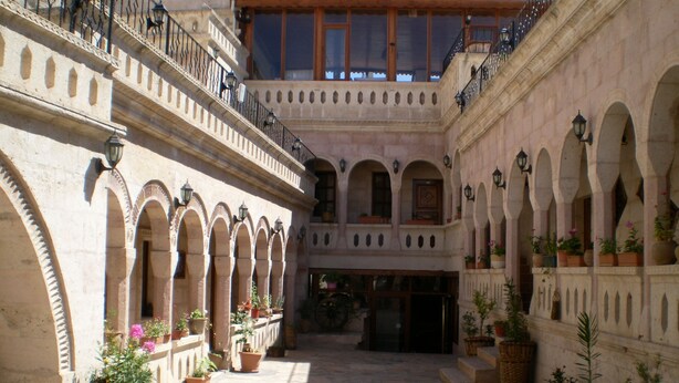 A courtyard with stone flooring, arched balconies, and potted plants. - Nature Park Cave Hotel (Nevsehir)