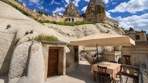 A stone building with a wooden door, outdoor seating with a table and chairs, and a staircase leading to a higher level. - Nature Park Cave Hotel (Nevsehir)