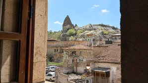 A view through a window of a building with a stone facade, a courtyard with parked cars, and a mountain with a prominent peak in the background. - Nature Park Cave Hotel (Nevsehir)