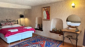 A bedroom with a bed, a bedside table, a mirror, a rug, and a wall-mounted shelf. - Nature Park Cave Hotel (Nevsehir)