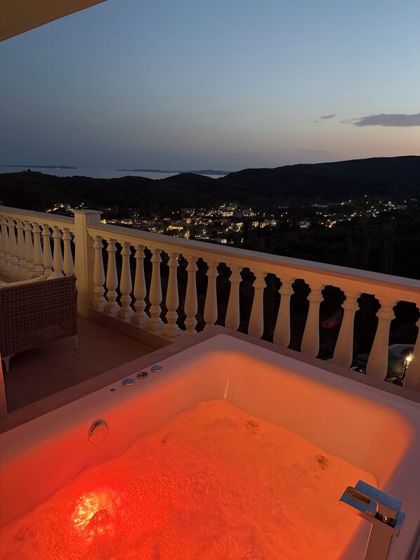 A balcony with a hot tub, white balustrade, and a view of a town at dusk.