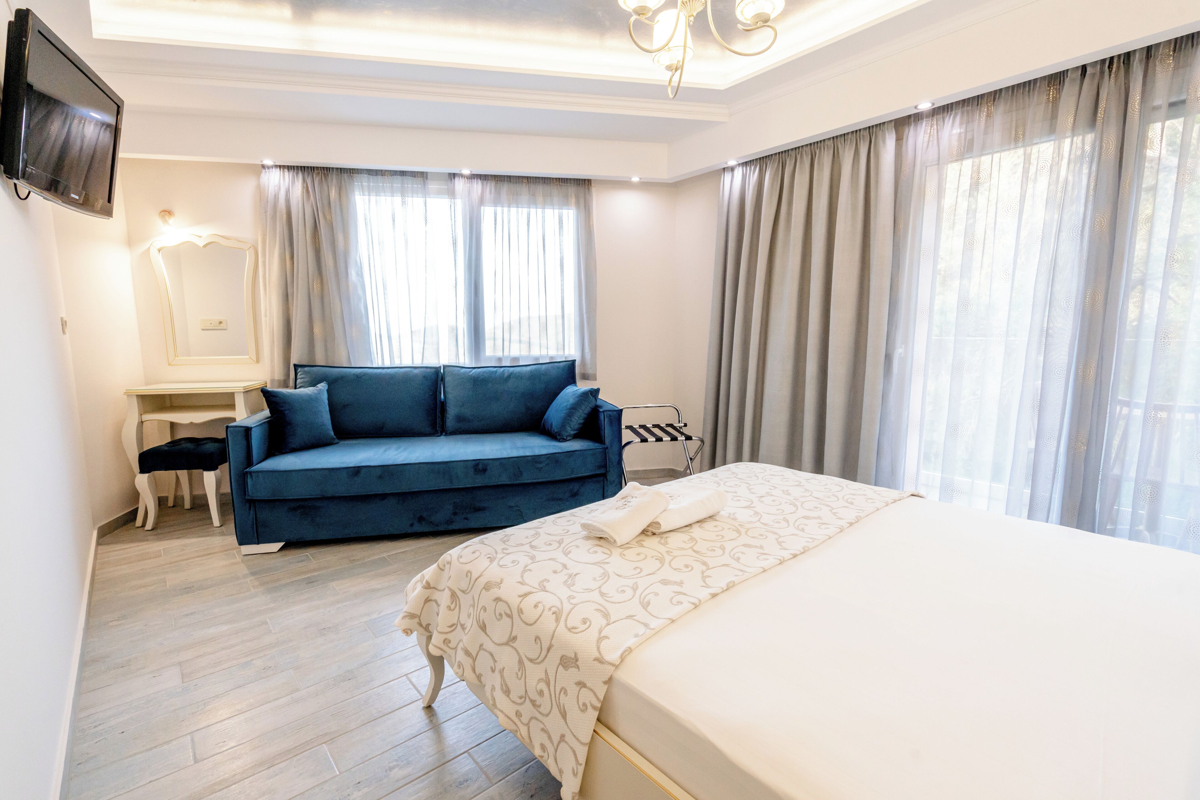 A hotel room with a large bed, a blue sofa, a desk with a chair, and a TV mounted on the wall.