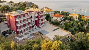 Un edificio de varios pisos con balcones, una terraza en la azotea y vista al mar con barcos.