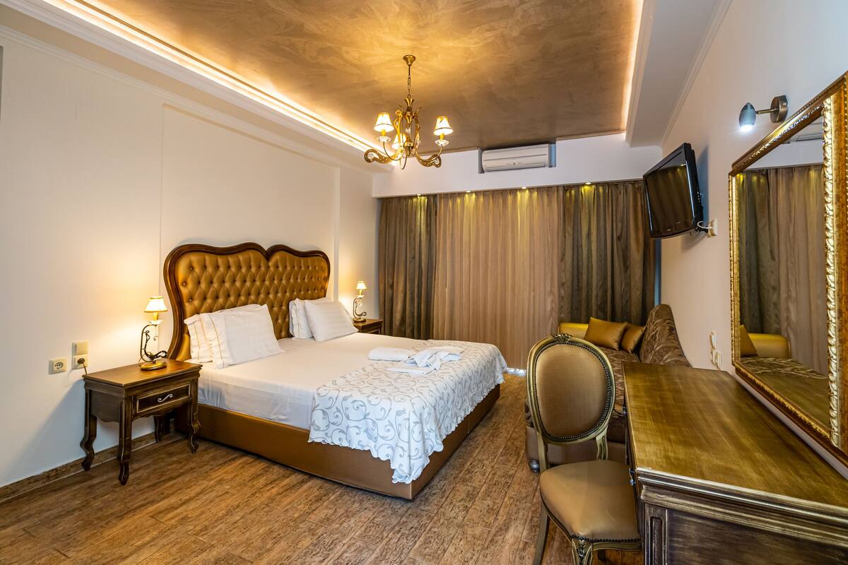Una habitación de hotel con una cama grande, un escritorio, una silla, un televisor y una araña.