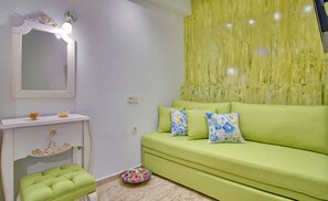 Une pièce avec un canapé vert, une coiffeuse blanche avec un miroir et un bol décoratif posé sur le sol.