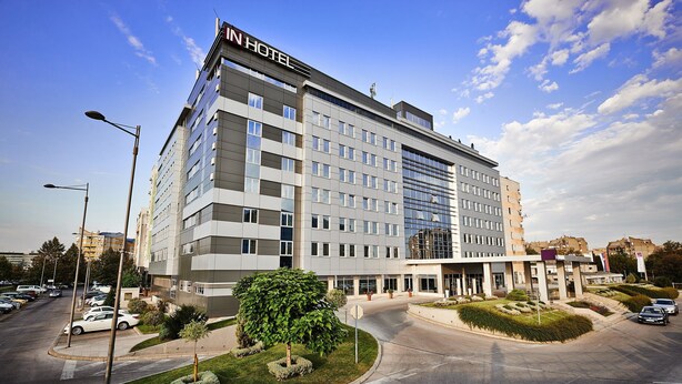 A modern hotel with a prominent "IN HOTEL" sign, a spacious parking lot, and well-maintained landscaping.