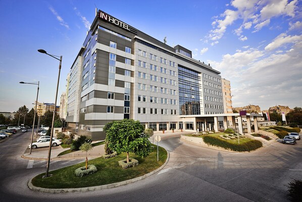 A modern hotel with a prominent "IN HOTEL" sign, a spacious parking lot, and well-maintained landscaping.