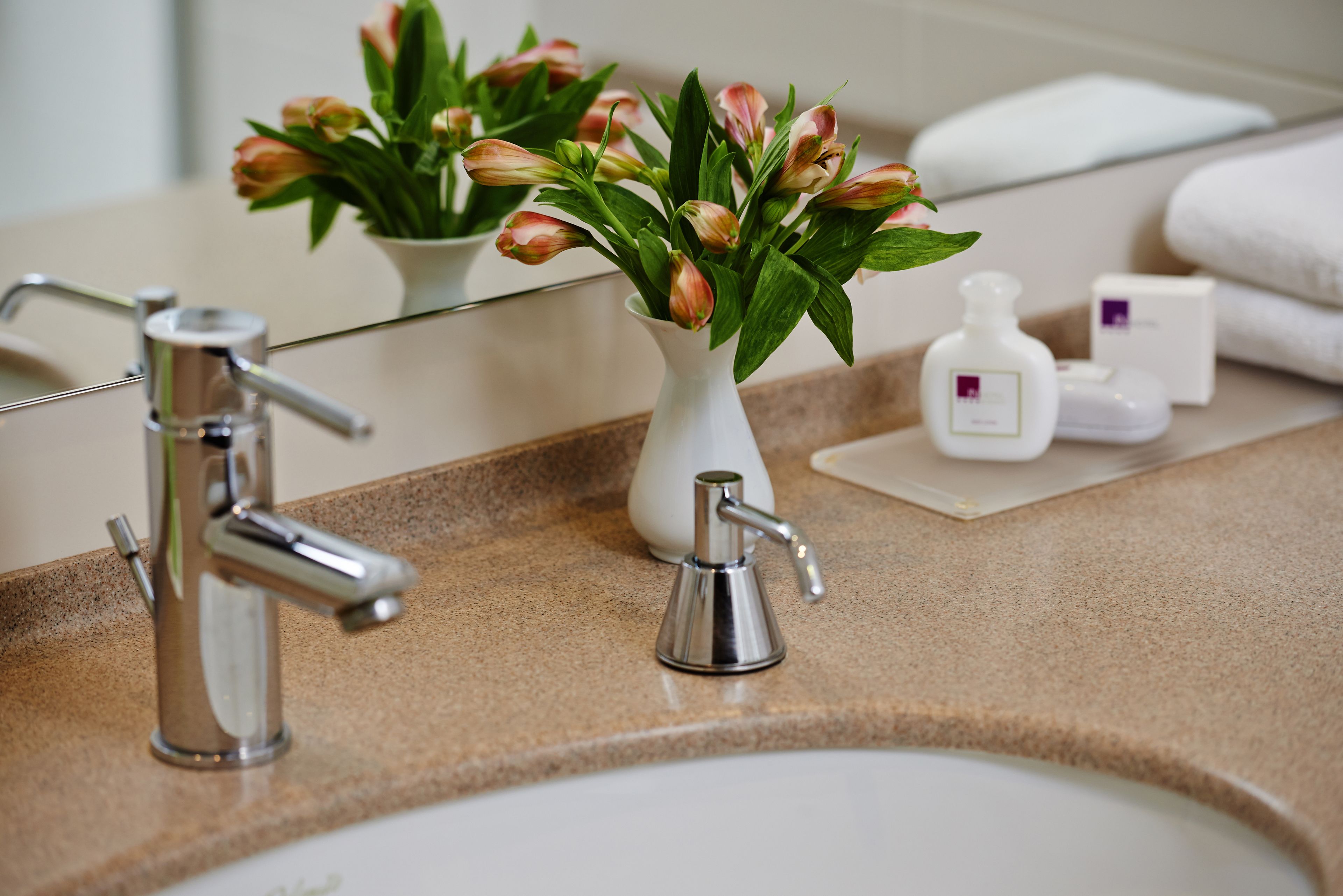 A bathroom vanity with a sink, mirror, and a vase of flowers.
