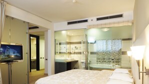 A hotel room with a bed, a TV, a bathroom with a shower, and a desk with a phone.