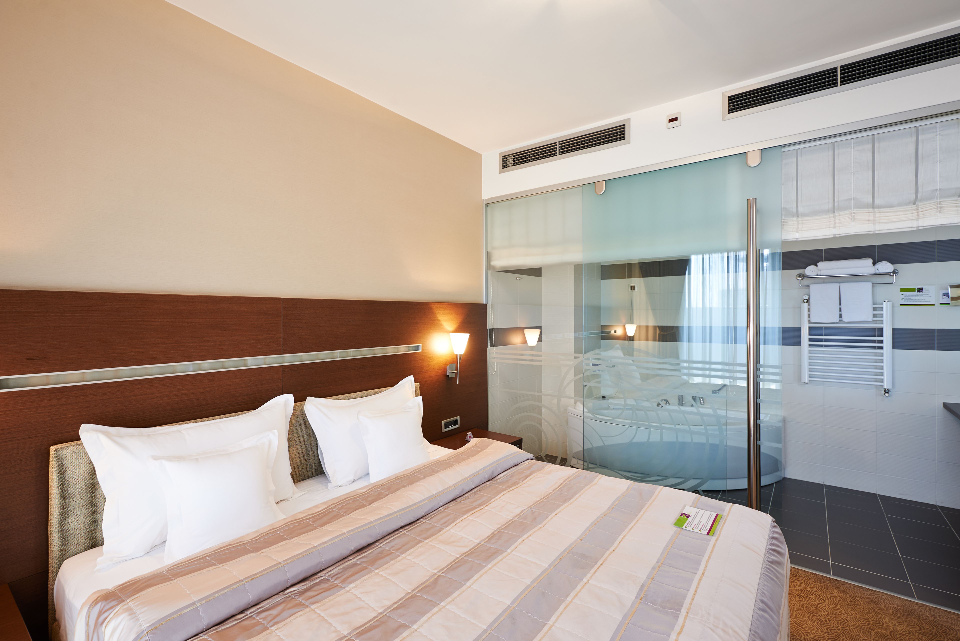 Habitación de hotel con cama, mesita de noche, cabina de ducha de vidrio y toallero de pared.
