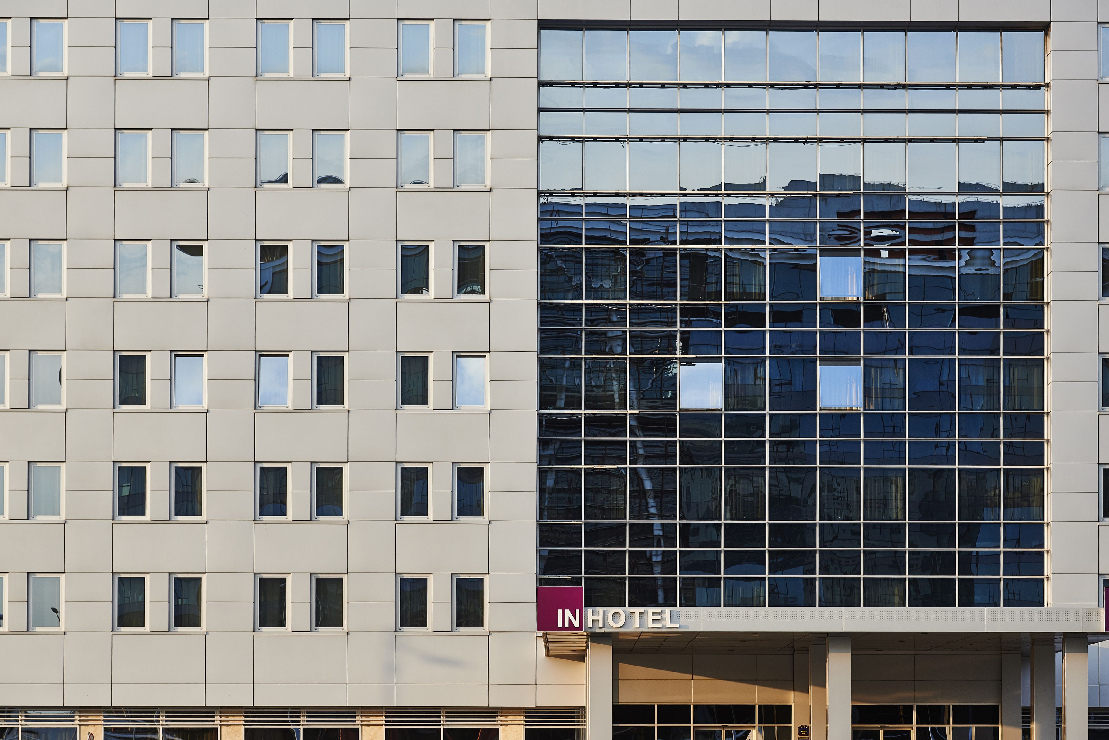 En modern hotellbyggnad med en reflekterande glasfasad och en skylt med texten ”IN HOTEL”.
