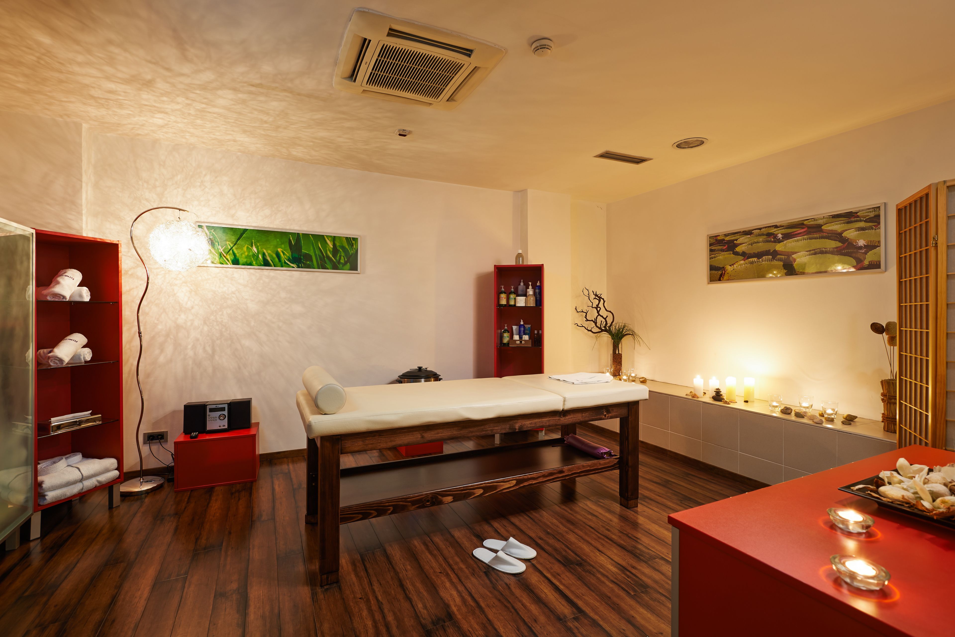 A spa room with a wooden bench, a red cabinet, and a wall-mounted shelf with bottles.