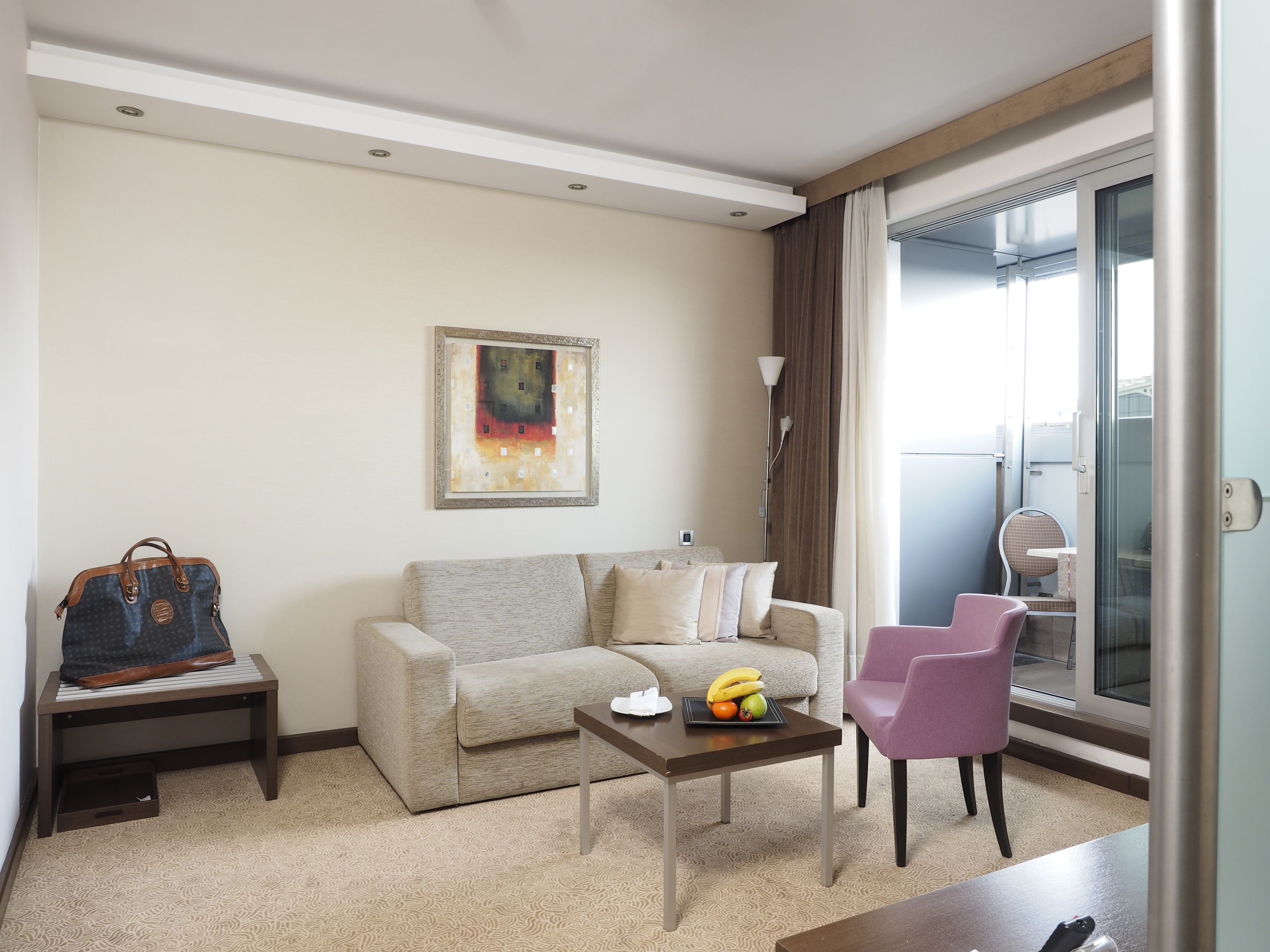 A living room with a sofa, a coffee table with fruit, a purple chair, and a bag on a bench.