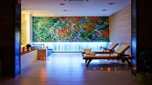 Zona de spa con un gran mural, dos sillones de descanso, una planta pequeña y una fuente de agua.