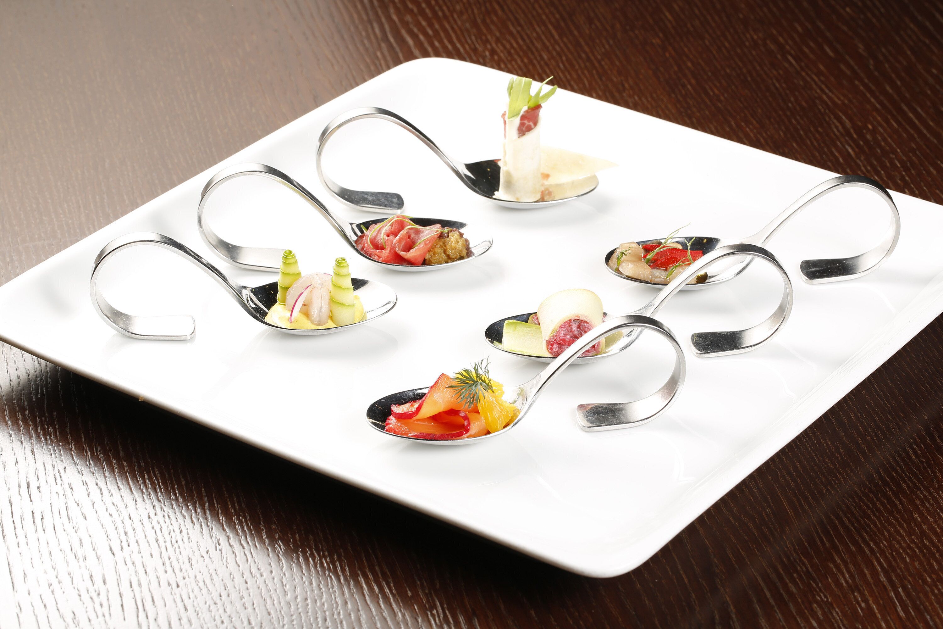 A white rectangular plate with six spoons containing various food items.