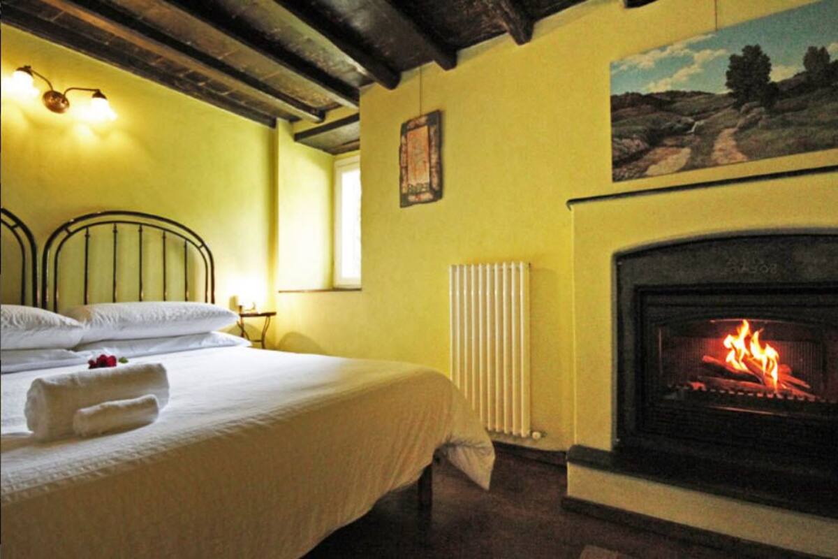 A room with a bed, a fireplace, a painting on the wall, and a window.