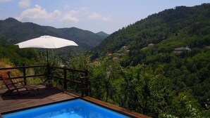A swimming pool with a wooden deck, a wooden chair, and an umbrella. - Agriturismo Casa del Bosco (Borzonasca)