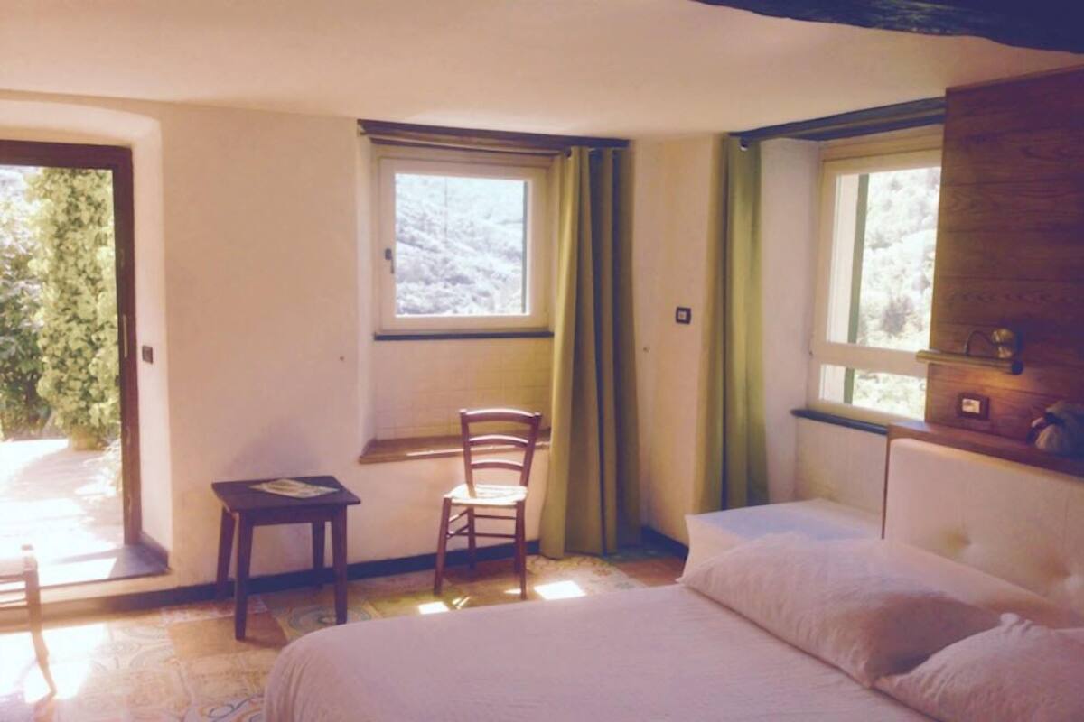 A bedroom with a bed, a chair, a small table, and a window.