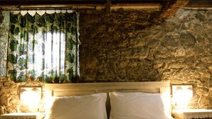 A bed with white linens in a room with stone walls and a window with green foliage. - Agriturismo Casa del Bosco (Borzonasca)