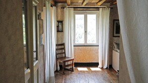 A room with wooden flooring, a wooden chair, a window with curtains, and a radiator. - Agriturismo Casa del Bosco (Borzonasca)