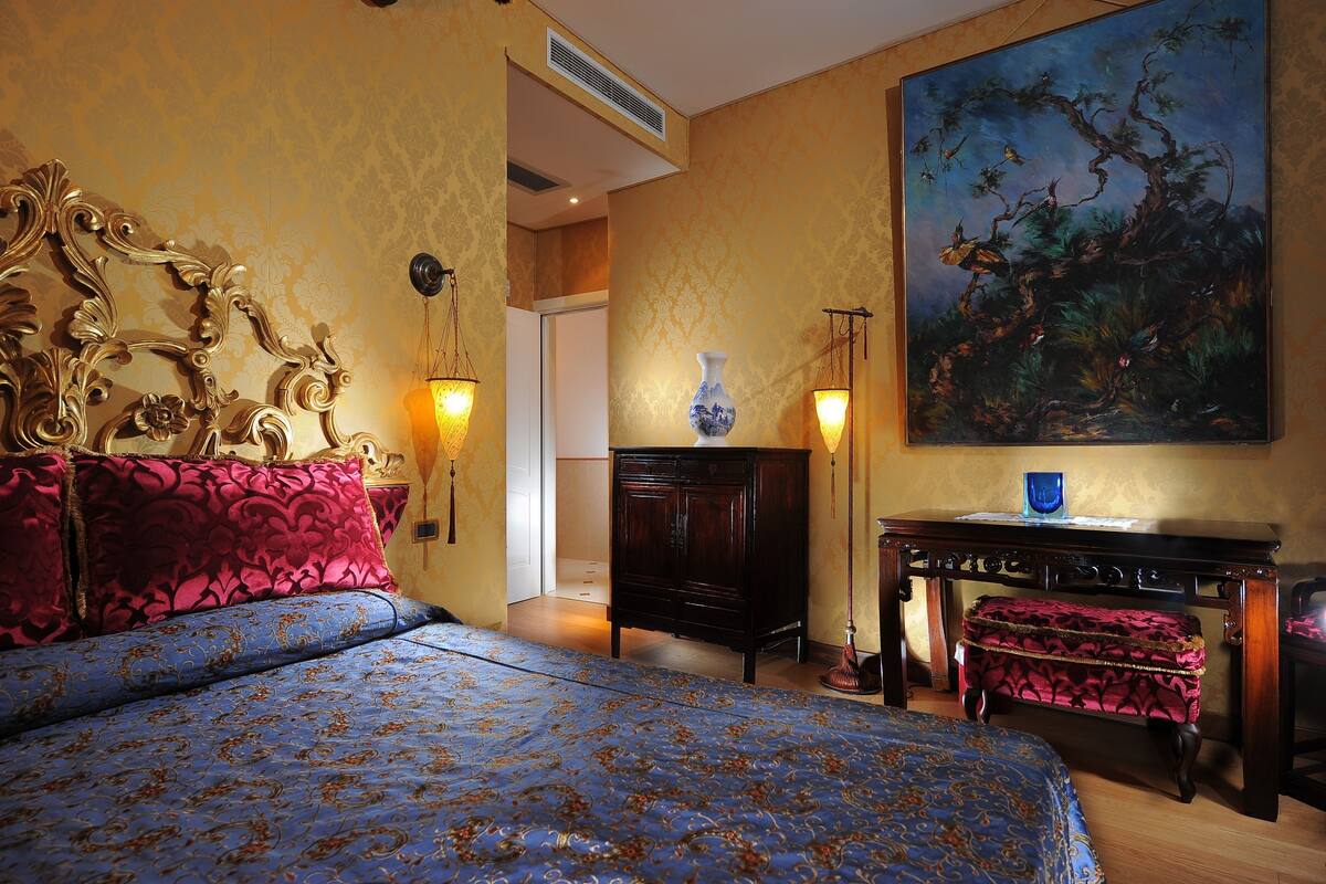 Une chambre avec un grand lit, une commode, un tableau accroché au mur et deux lampes fixées au mur.