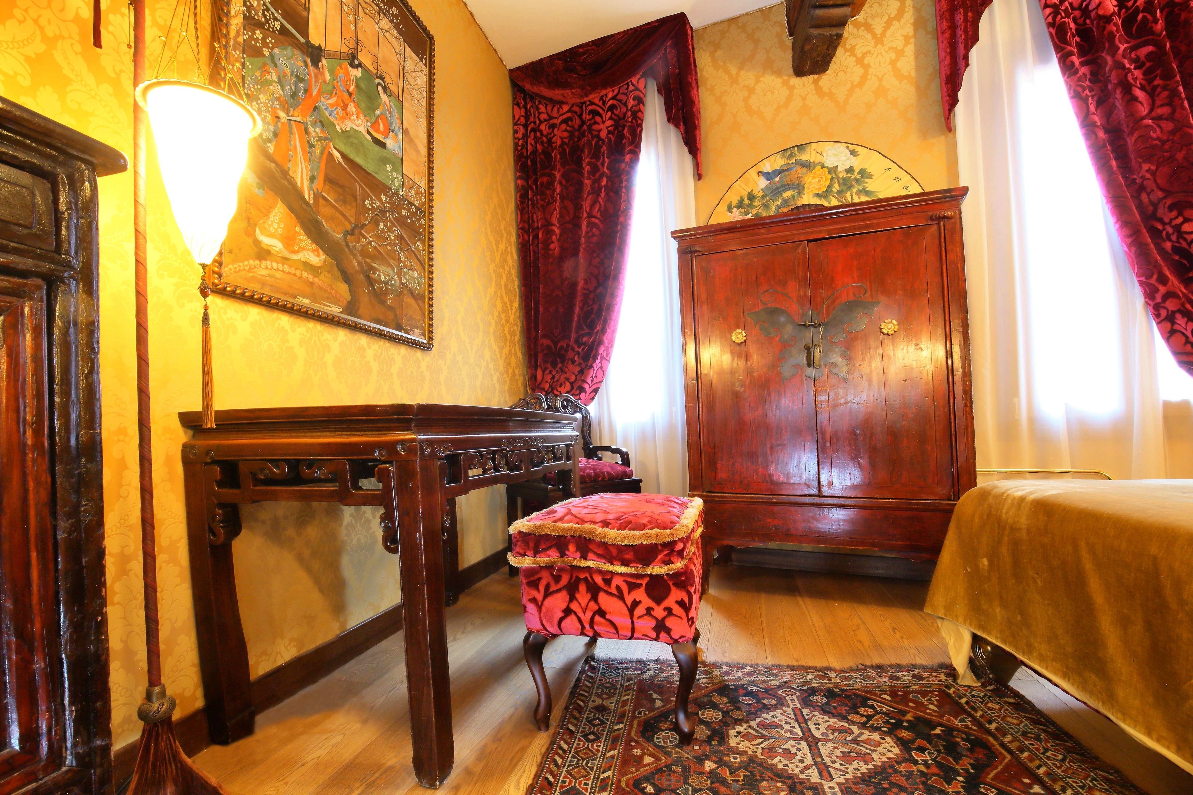 Una habitación tradicional con un escritorio de madera, un taburete acolchado rojo, un armario de madera grande y una alfombra estampada.