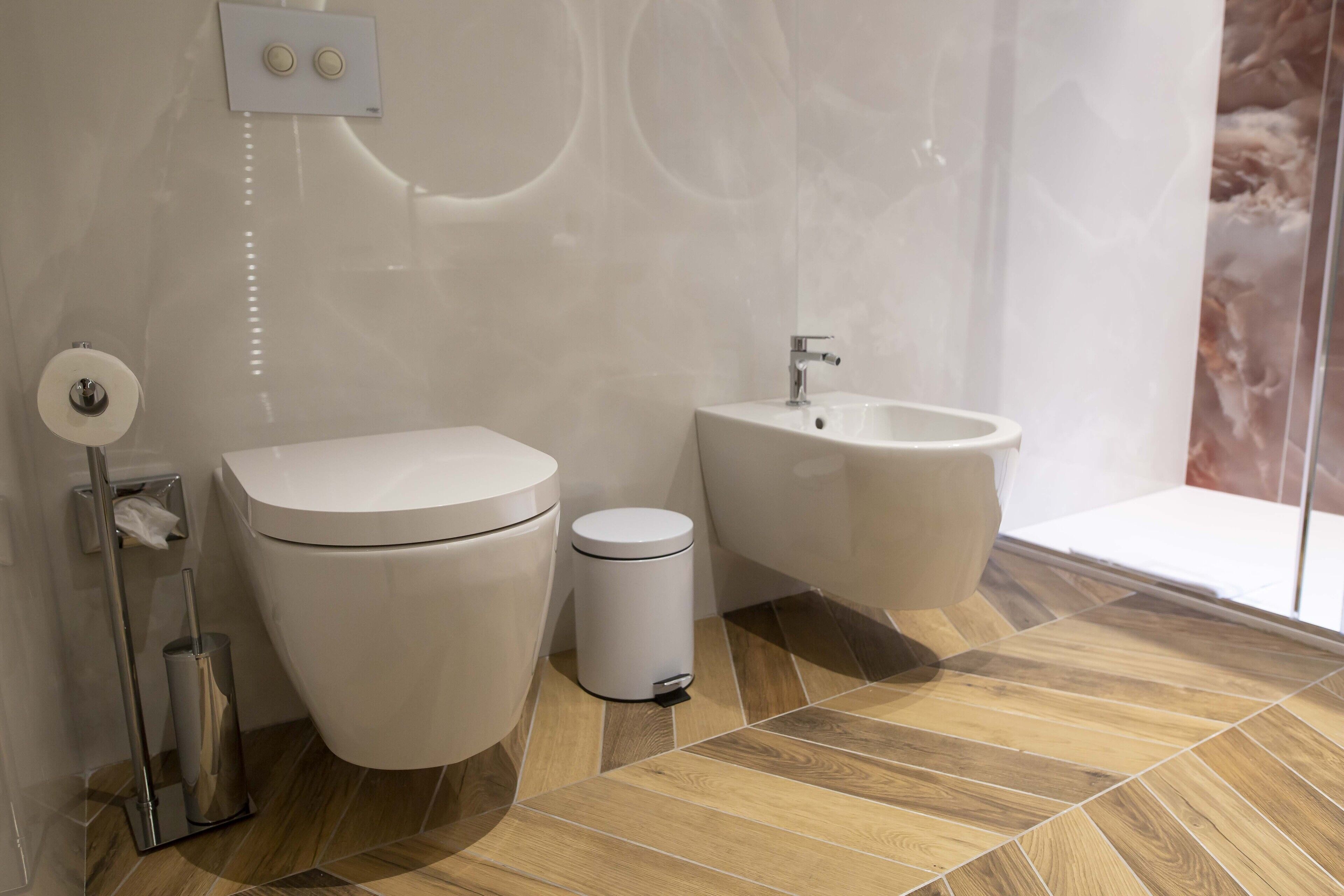 Ein modernes Badezimmer mit Toilette, Bidet und Waschbecken, mit Holzboden und Marmorwand.