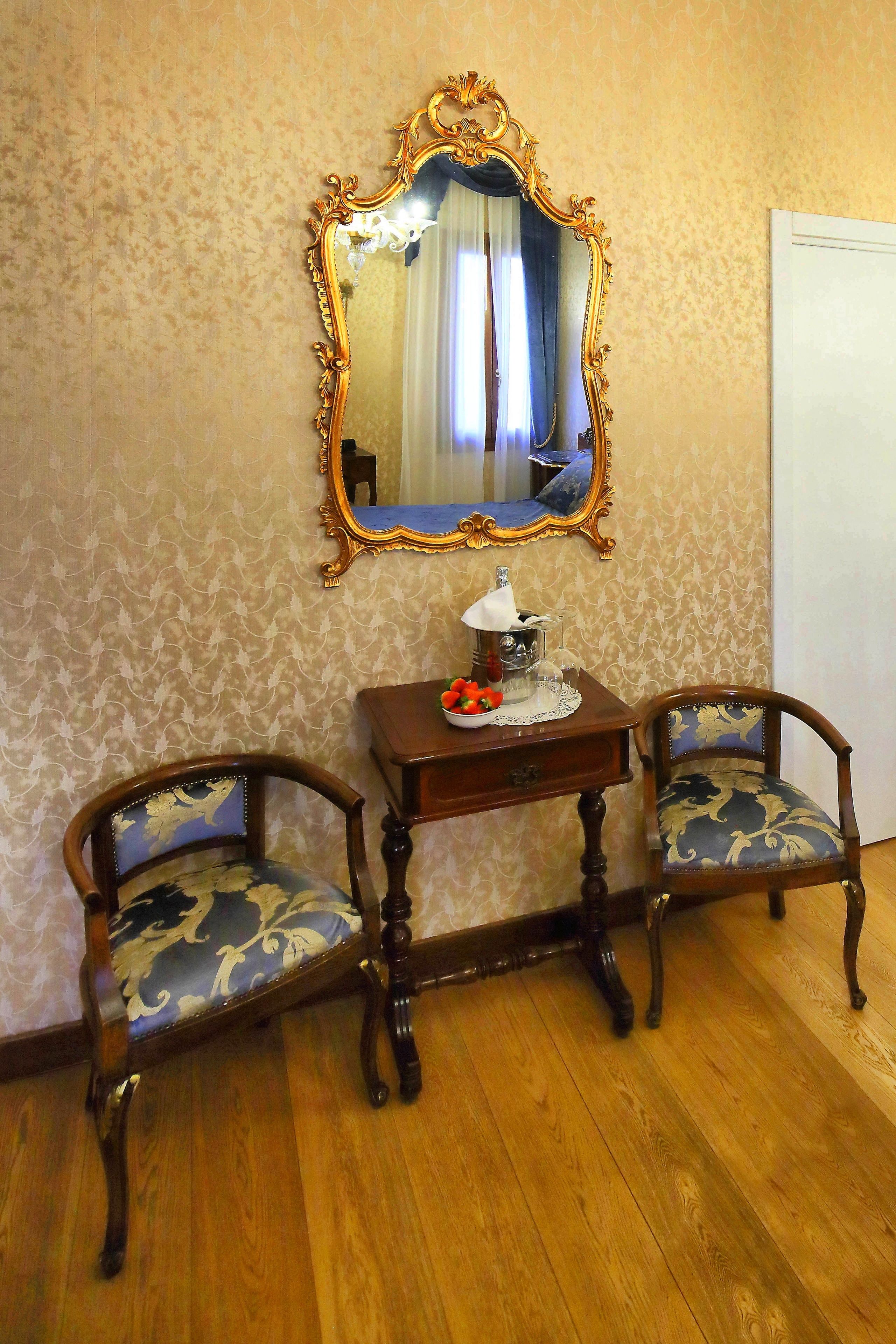 A room with two ornate chairs, a small table with a decorative item, and a mirror on the wall.