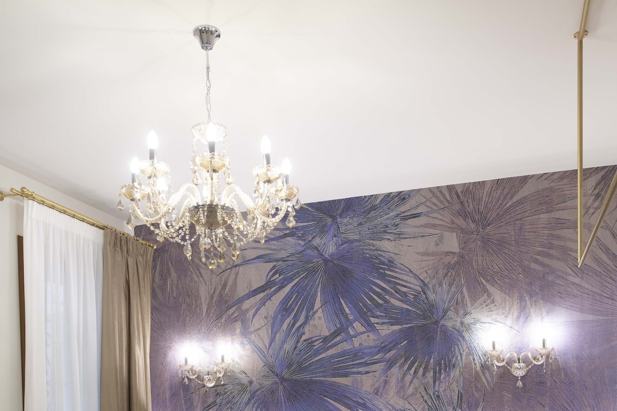 Une chambre d’hôtel avec un grand lit, un lustre, une tête de lit dotée d’un éclairage intégré, une fresque murale et un téléphone sur la table de chevet.