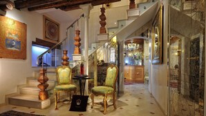 Un magnifique escalier orné de balustrades travaillées, un lustre et un coin salon avec des fauteuils de style vintage.