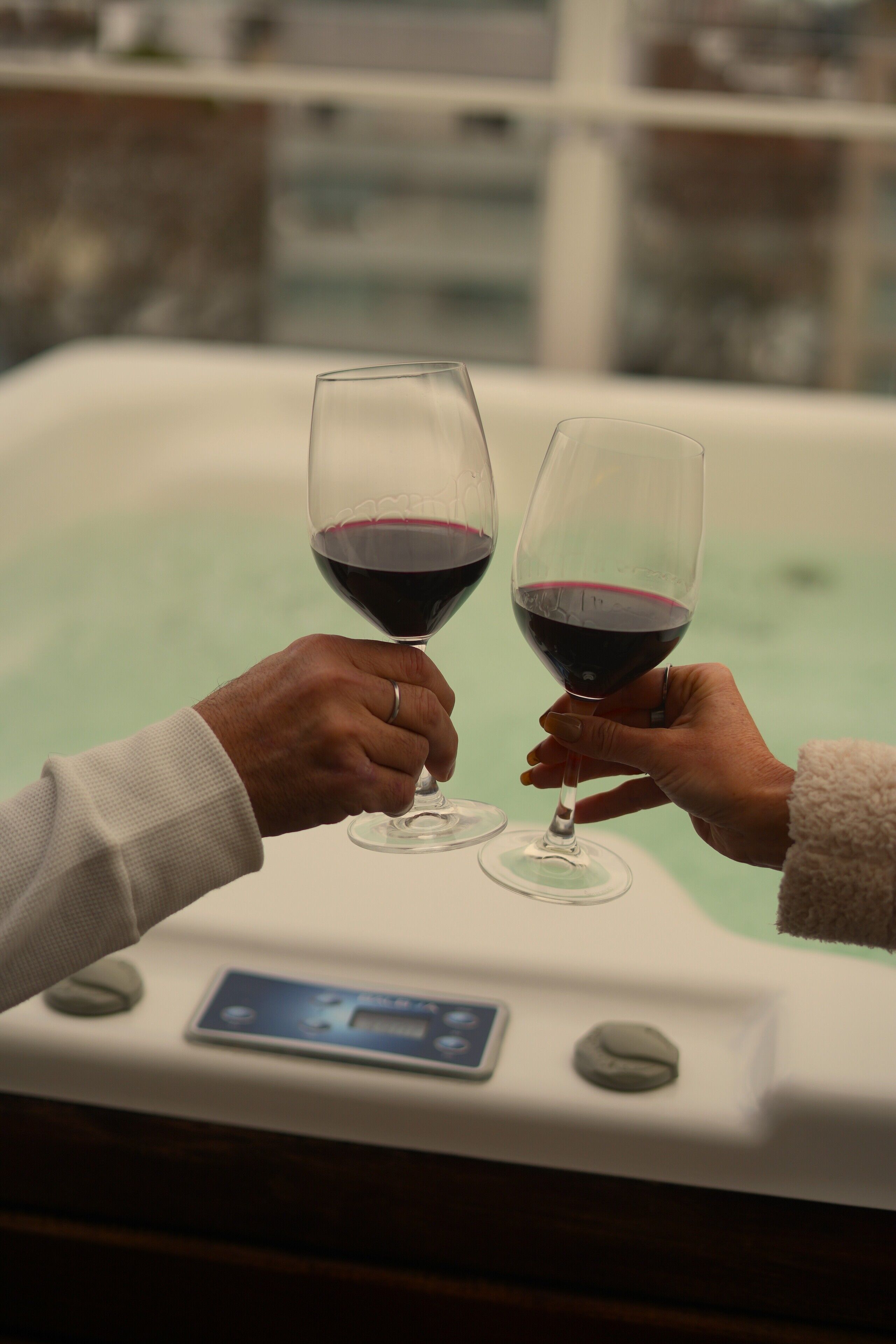 Two hands holding wine glasses in a jacuzzi tub.