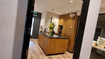 Een modern receptiegebied met een houten receptiebalie, een vaas met gele bloemen en een houten wandpaneel.