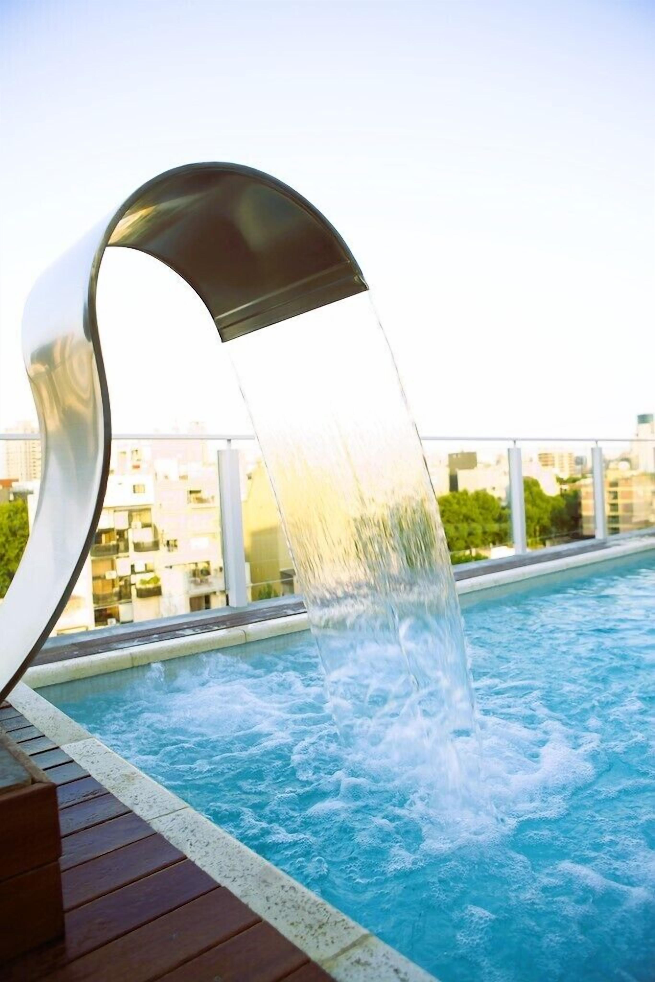 A modern outdoor swimming pool with a water feature.