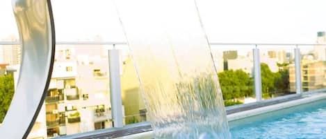 A modern outdoor swimming pool with a water feature.