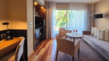 A hotel room with a dining area, a sofa, and a view of greenery outside.