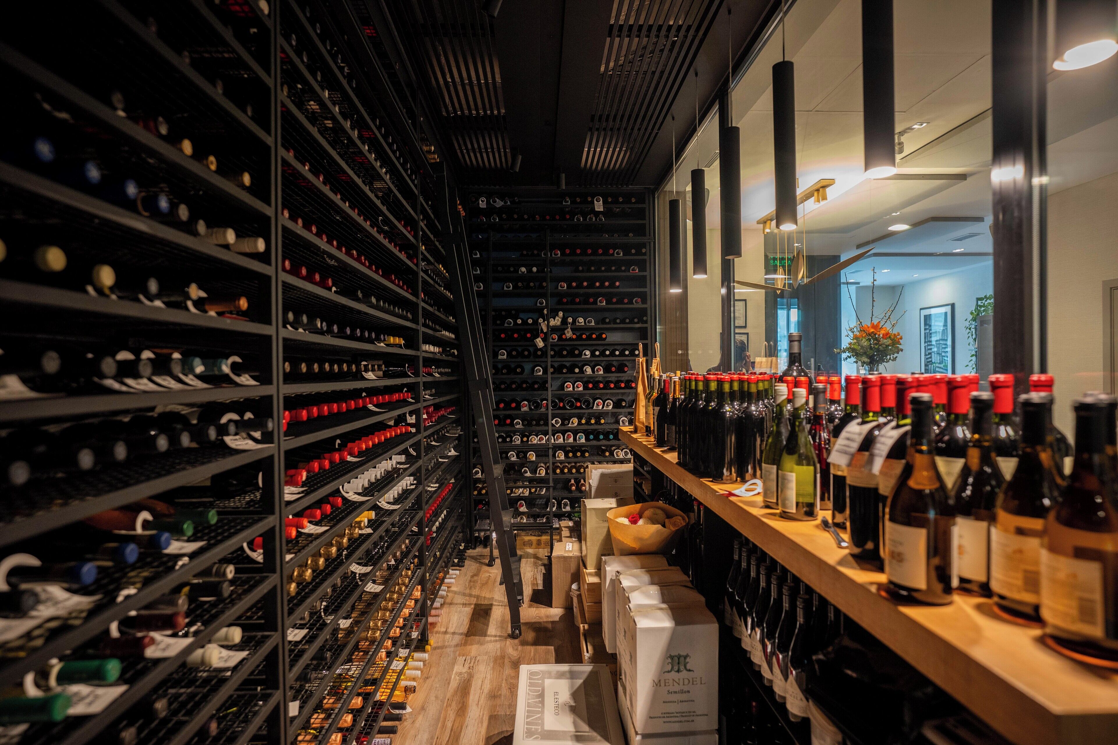A wine cellar with shelves of wine bottles and a wooden counter with more bottles.