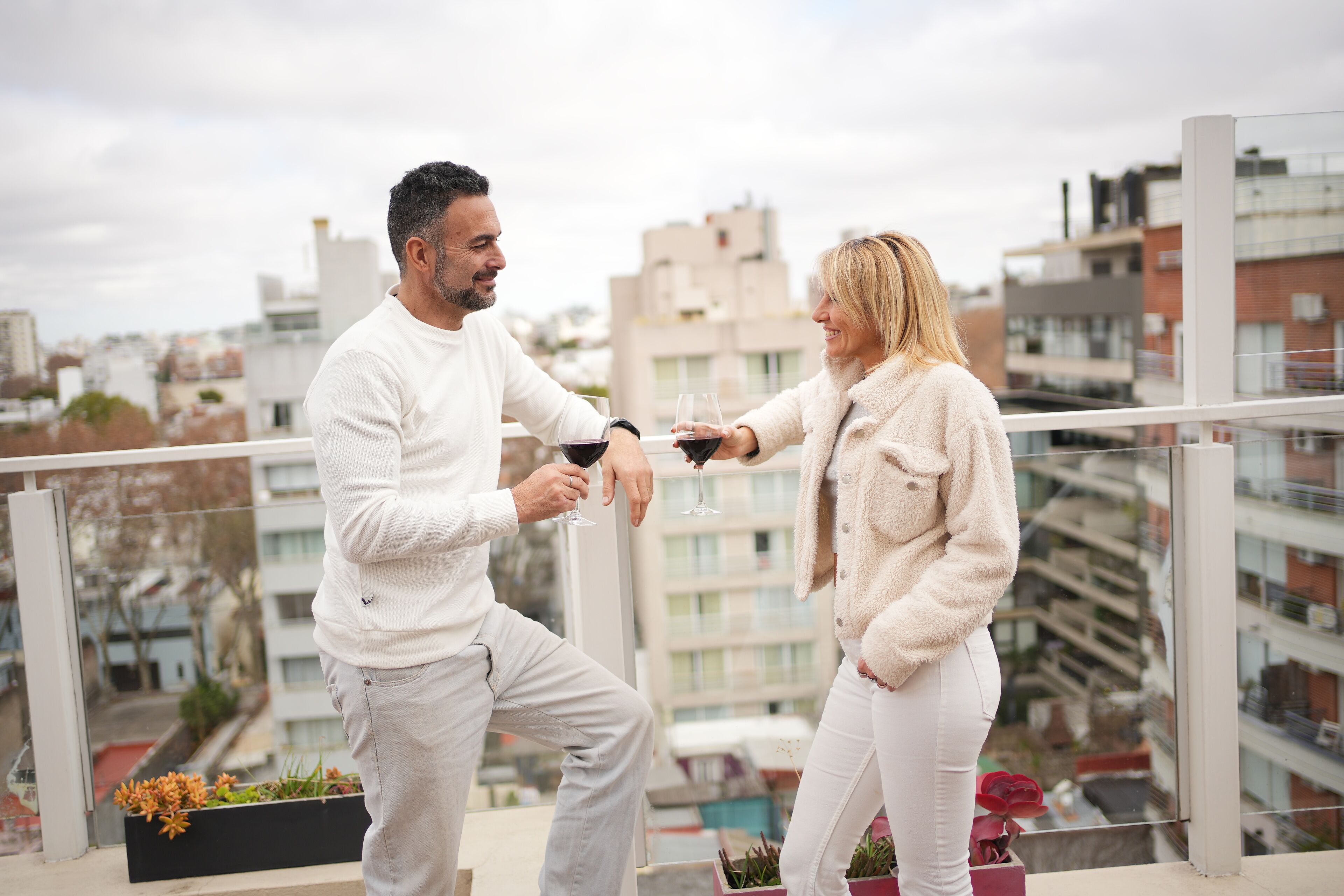 Una pareja brindando con copas de vino en un balcón con vista a la ciudad.