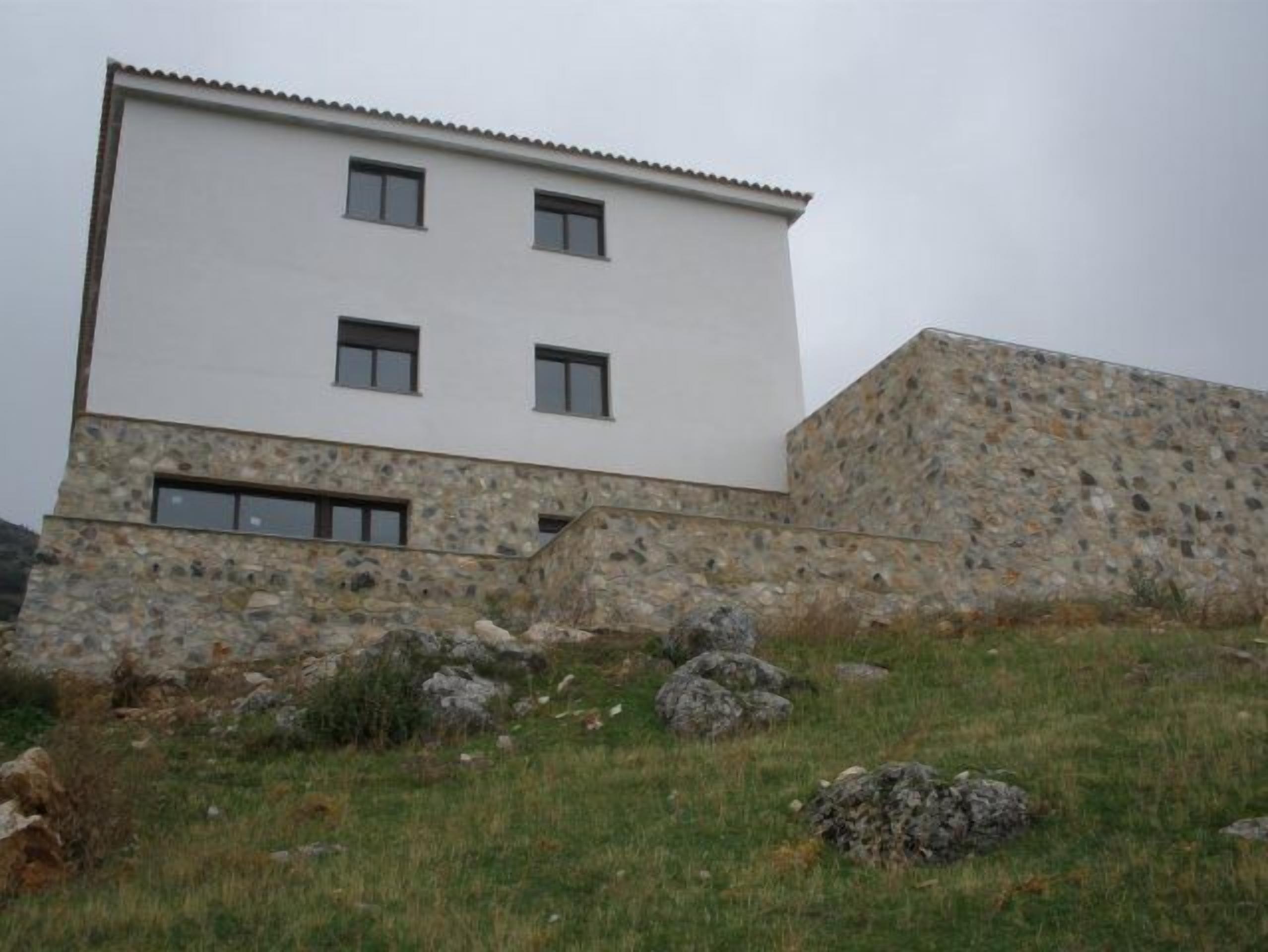 A modern building with a flat roof, a stone facade, and a small window on the ground floor.