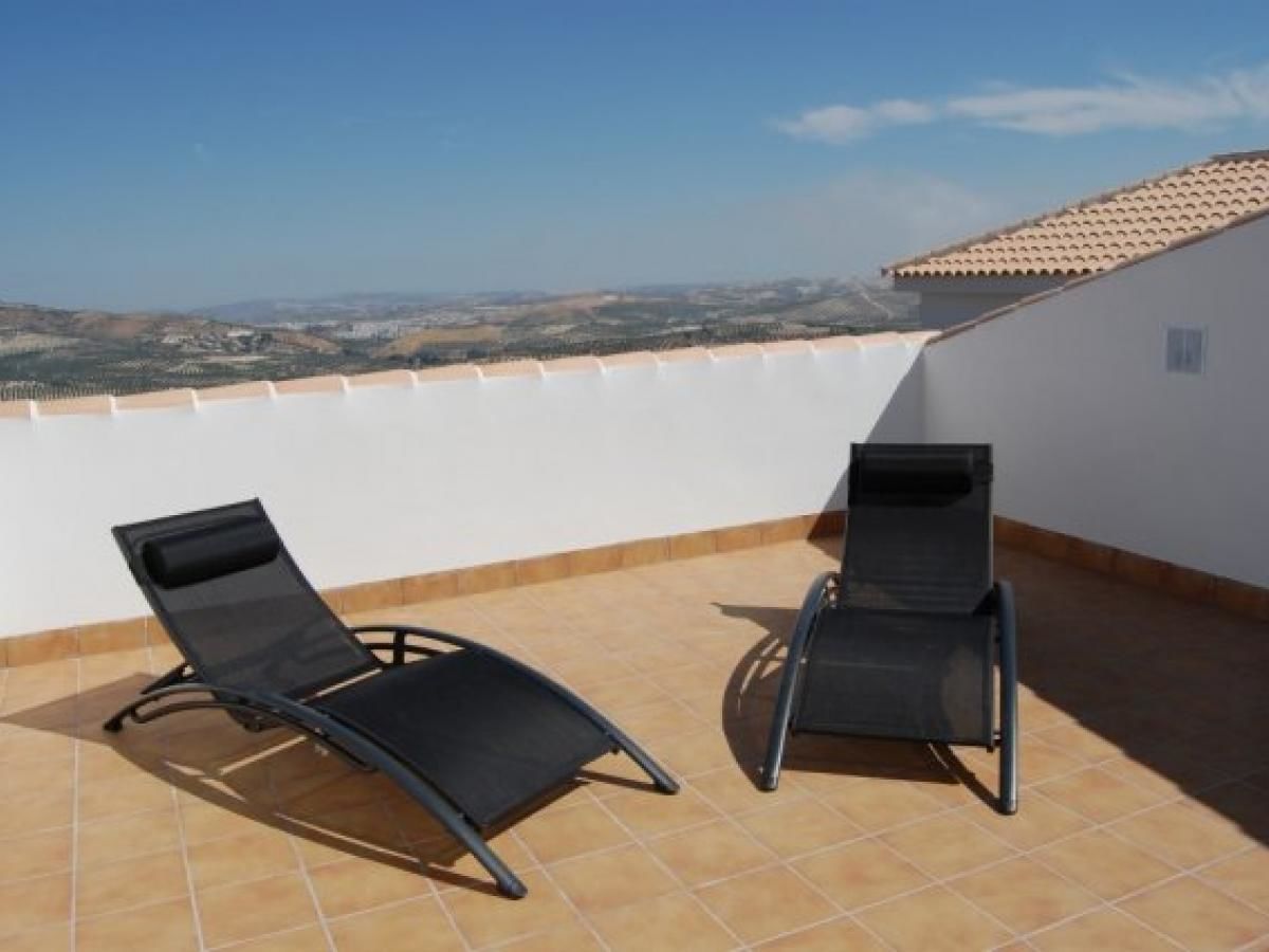 Terraza en la azotea con dos sillones negros y una pared blanca.