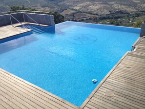 A rectangular swimming pool with a wooden deck surrounding it. - Los Castillarejos Apartamentos Rurales (Luque)
