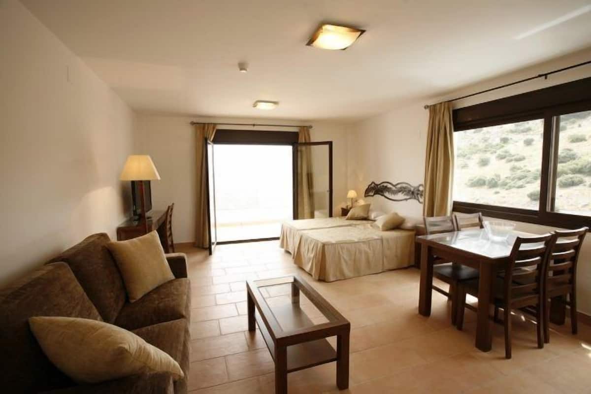A hotel room with a bed, a dining table with chairs, a sofa, and a lamp.
