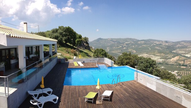 Ein Pool auf dem Dach mit Holzterrasse und Liegestühlen, mit Blick auf eine gebirgige Landschaft.