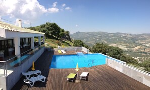 Piscina en la azotea con terraza de madera y sillones de descanso, con vista a un paisaje montañoso.