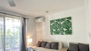 A modern living room with a ceiling fan, a sofa set, a dining area with chairs, and a large window with curtains. - Chevron Palms Holiday Apartments by Gold Coast Premium (Surfers Paradise)