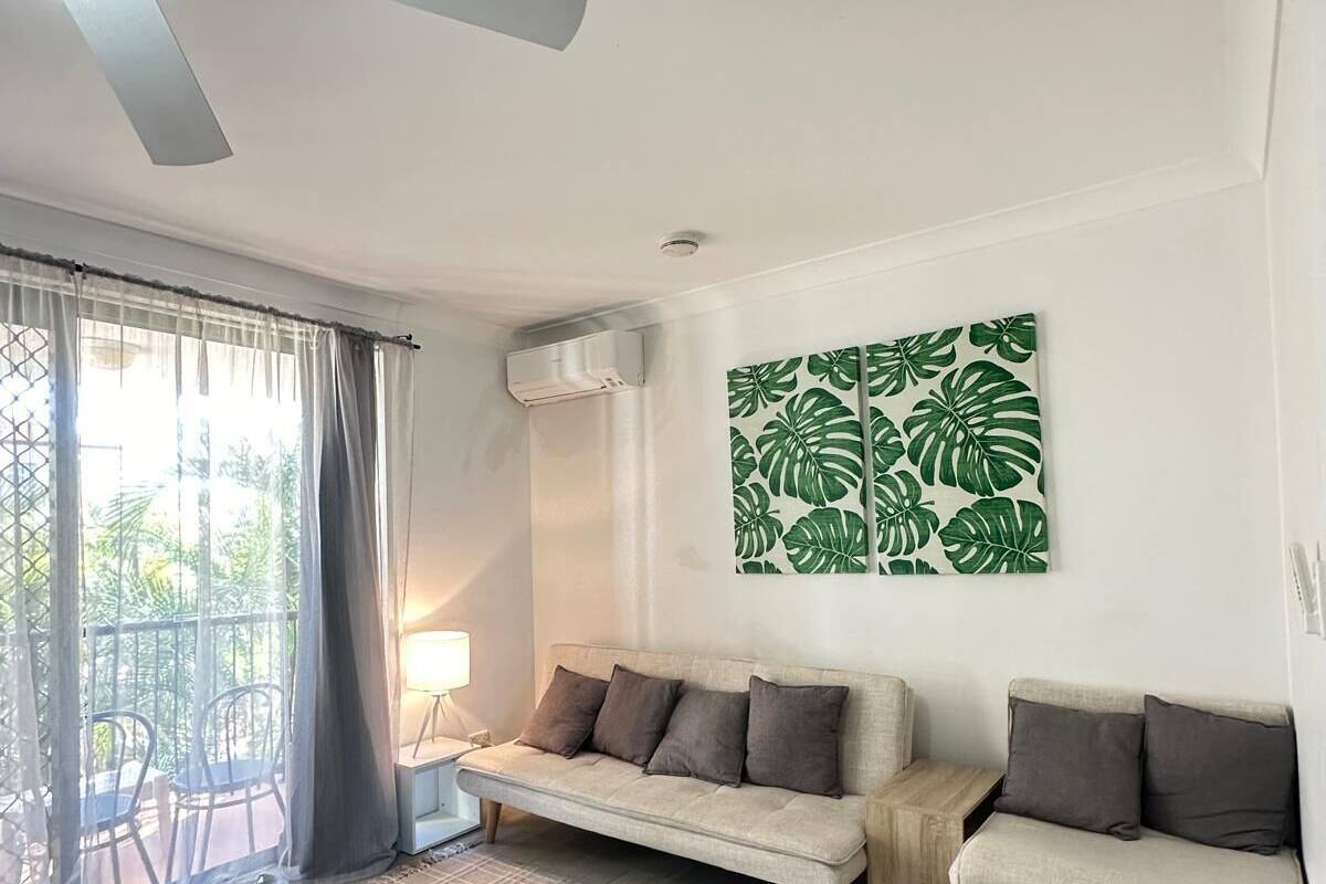 Una sala de estar moderna con ventilador de techo, un conjunto de sofás, un comedor con sillas y un ventanal con cortinas.
