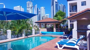 A swimming pool with lounge chairs, a gazebo, and a city skyline in the background. - Chevron Palms Holiday Apartments by Gold Coast Premium (Surfers Paradise)