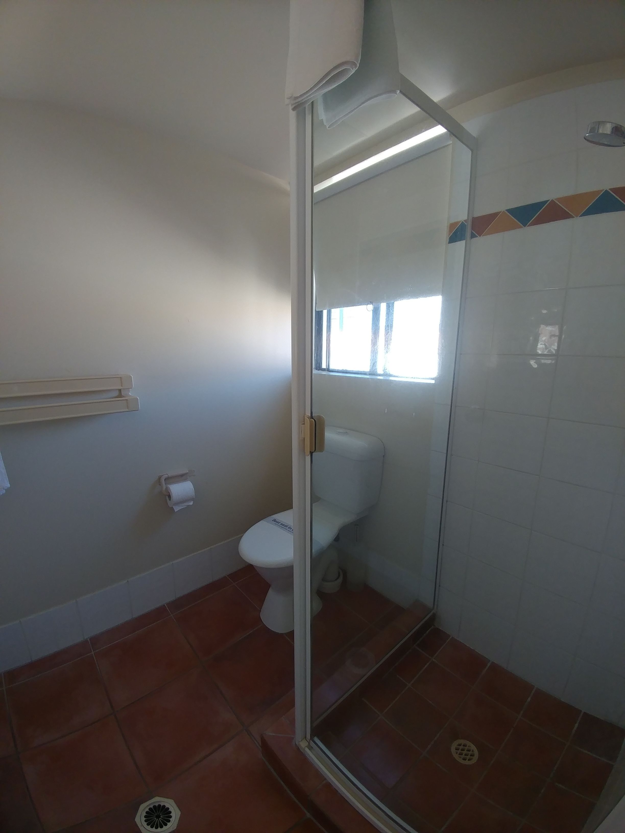 Ein Badezimmer mit Toilette, einer Duschkabine aus Glas und einem Fenster.